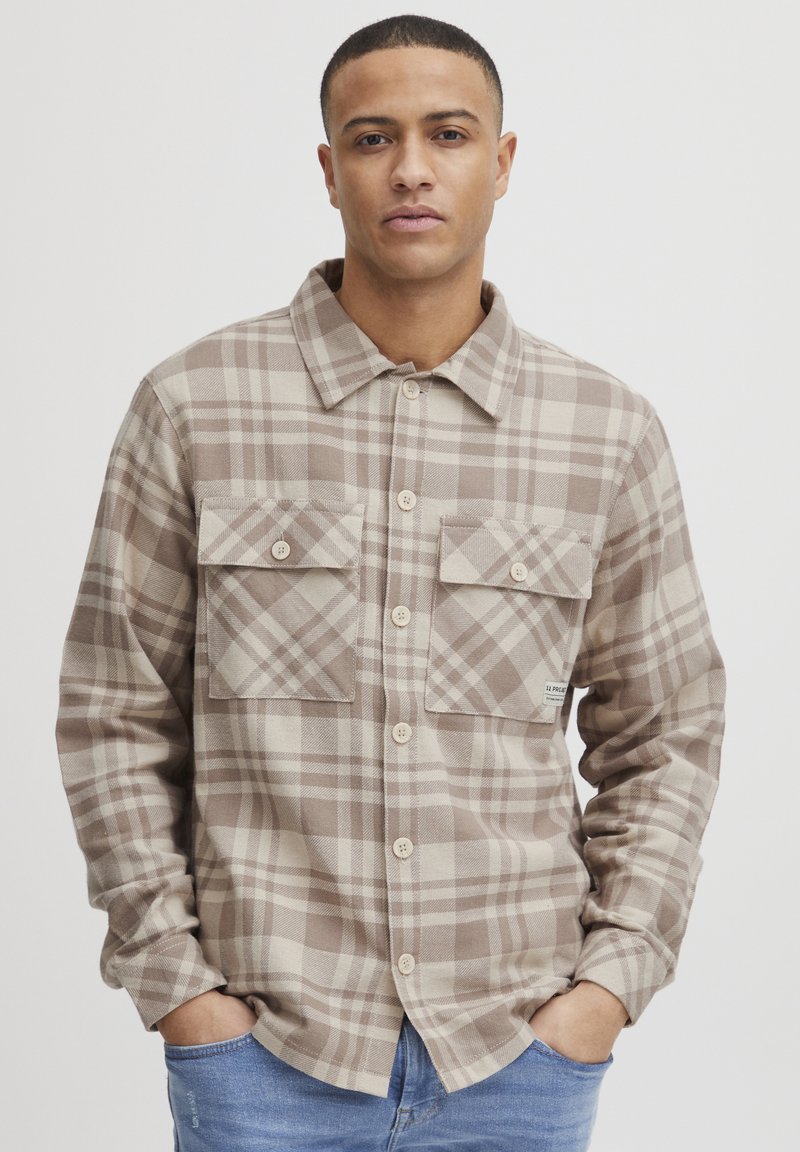 Brun og creme ternet flannel skjorte med krave, to brystlommer og knapper foran. Teksturert stof og løs pasform.