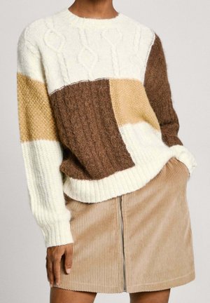 Osoba nosząca sweter typu color-block w kolorach białym, brązowym i beżowym, zestawiony z beżową spódnicą sztruksową z zamkiem z przodu.