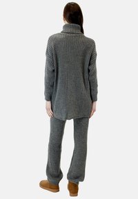 Suéter de punto gris acanalado con un cuello alto, combinado con pantalones acanalados a juego y botas de color beige, mostrando un ajuste relajado y textura.