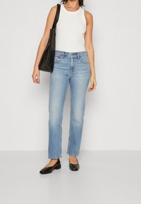 Vit ribbad linne, medelblå raka jeans och svarta platta skor. Modellen håller en svart tote-väska. Enkel, avslappnad outfit.