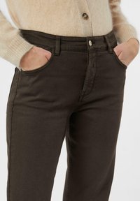 Bruine denim jeans met een aangesloten taille, voorzakken en een gladde textuur, gecombineerd met een lichtbeige, pluizige cardigan.