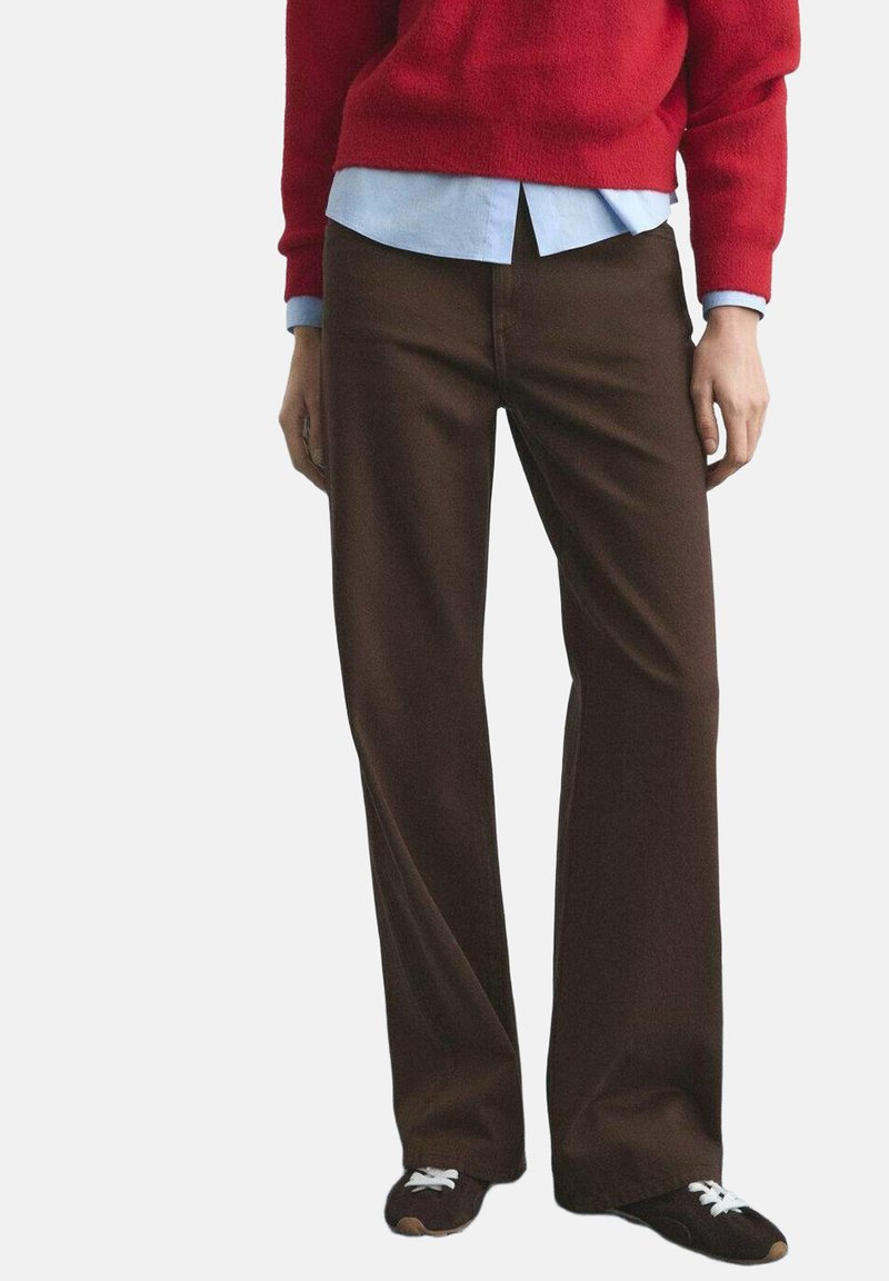 Pantalon marron à jambes larges en tissu texturé, associé à un pull rouge et une chemise bleu clair, complété par des chaussures foncées.