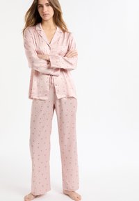 Jasnoróżowy zestaw piżamowy w paski i z motywem kwiatowym. Góra z kołnierzykiem, guzikami i kieszenią; spodnie o luźnym kroju.