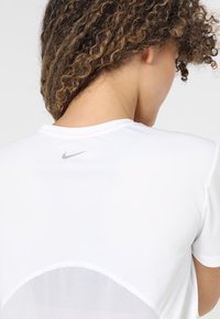 Camiseta blanca de Nike con escote redondo, mangas cortas y panel de malla en la espalda; presenta un pequeño logo gris en la nuca.