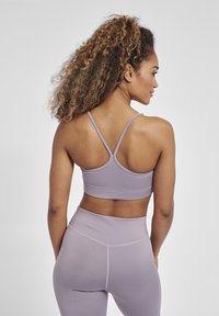 Lichtpaarse sportbh met dunne bandjes en een aansluitend ontwerp, in combinatie met bijpassende high-waisted leggings met een gladde textuur.