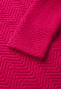 Fuchsia vadderad tyg med ett fiskbensmönster, slät textur och en vikning som visar sömdetaljer.