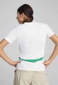 White athletic shirt with short sleeves and a green accent band around the waist. Textured fabric, fitted design, and crew neckline.