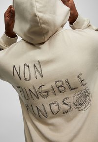Beżowa bluza z kapturem ze sznurkiem, z czarnym haftowanym napisem "NON FUNGIBLE MINDS" i okrągłym rysunkiem na plecach.