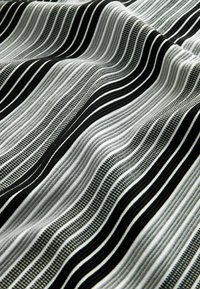 Tela a rayas en blanco y negro con líneas onduladas. Superficie texturizada, alternando áreas suaves y acanaladas, con finas franjas y un aspecto suave.