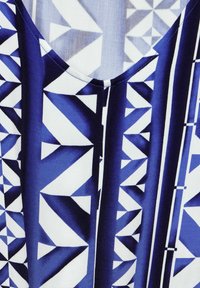 Tissu bleu et blanc avec des motifs géométriques comprenant des triangles et des rectangles. Encolure arrondie avec une texture lisse et des détails de motif clairs.