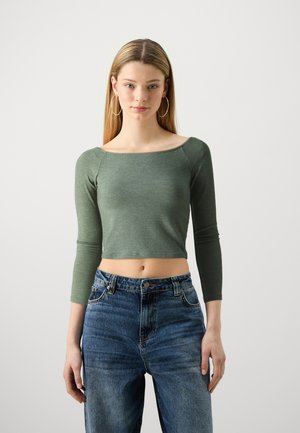 Green, fitted, long-sleeve crop top with a square neckline; paired with high-waisted, faded blue jeans featuring stitching details.