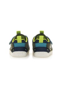 Zapatos de tela verdes y marino con acentos azules, correa de velcro y suela de goma. Presentan bucles verdes brillantes para fácil calzado.