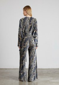 Mono con estampado floral en tejido texturizado, con mangas largas, cintura ceñida y pantalones de pierna ancha en tonos de azul y dorado.