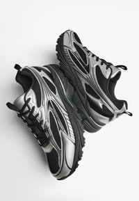 Crne i srebrne atletske tenisice s gornjim dijelom od mrežaste tkanine i sintetičkih materijala, teksturiranim potplatima i istaknutim detaljima duž bokova i na vrhovima.