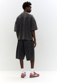 T-shirt grigia oversize e pantaloni corti abbinati, realizzati con un tessuto simile al denim, caratterizzati da una vestibilità rilassata e dettagli di cucitura visibili.