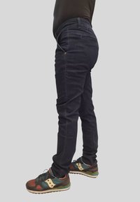 Jeans aderenti di colore blu scuro con vita bassa, dotati di una tasca per monete e dettagli di cucitura sottili, abbinati a scarpe sportive multicolori.