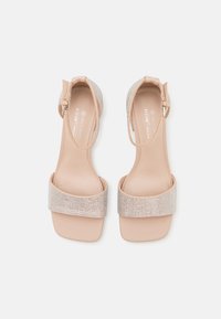 Sandales en cuir vegan couleur nude avec une bande métallisées texturée, bout ouvert et bride à la cheville. Talons carrés et semelle intérieure lisse.