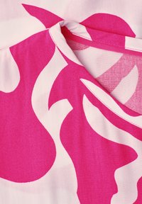 Gros plan d'un tissu rose et blanc à motifs avec un col arrondi et des coutures détaillées sur un vêtement léger.