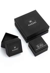 Schwarze Boxen mit dem "Kuzzoí"-Logo, in verschiedenen Größen; strukturierte Oberflächen; enthalten Etiketten, die recyceltes Material und Herkunft aus Deutschland anzeigen.