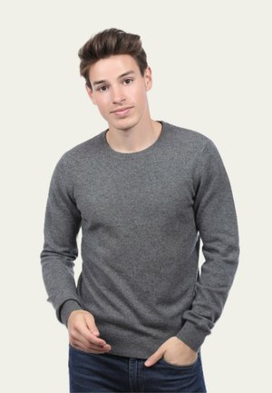 Pull gris en tissu doux et texturé. Doté d'un col ras du cou et de poignets et d'un ourlet côtelés. Porté avec un jean bleu.