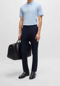 Polo bleu clair à manches courtes, pantalon bleu marine, sac en cuir noir et chaussures foncées, présentant des lignes épurées et un design minimaliste.