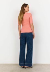 Light pink ribbed knit top with short sleeves paired with high-waisted, wide-leg blue denim jeans. Accented with black and white patterned shoes.