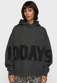 Grauer, übergroßer Kapuzenpullover aus weichem Material, mit großen schwarzen Buchstaben "100 DAYS" auf der Vorderseite und einer Kordelkapuze.