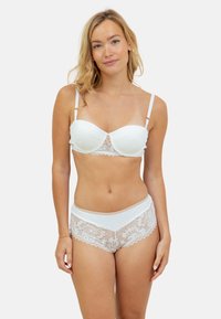 Un soutien-gorge en dentelle blanche et une culotte taille haute assortie présentent des motifs floraux, des tissus lisses, des bretelles réglables et des bords festonnés.