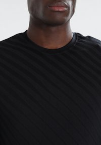 Musta lyhythihainen T-paita, jossa on teksturoitu vaakaraidoitus. Ominaisuuksina pyöreä kaula-aukko ja pehmeä, hengittävä kangas.