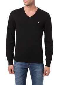 Maglione nero a v-collo realizzato in tessuto lavorato a maglia, con maniche lunghe, polsini a costine e un piccolo logo sul petto. Abbinato a jeans blu.