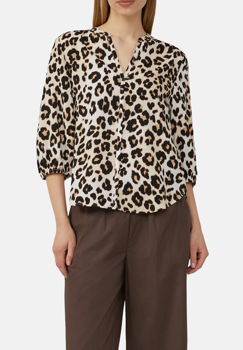 Bluse mit Leopardenmuster, V-Ausschnitt, 3/4 Puffärmeln und einem leichten, glänzenden Stoff. Kombiniert mit lockeren, braunen Hosen.