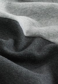 Weich gefalteter Stoff in hellen und dunklen Grautönen mit einer glatten, gestrickten Textur und subtilen Schatten, die die Falten hervorheben.