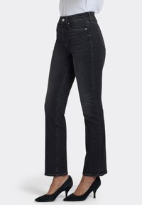 Svarta raka jeans i denim med hög midja, fem fickor och synliga sömmar, kombinerade med gröna högklackade skor.