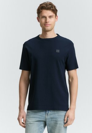 Navyblaues T-Shirt mit kurzen Ärmeln aus strukturiertem Stoff, rundem Ausschnitt und einem kleinen quadratischen Logopatch auf der Brust. Lockere Passform.
