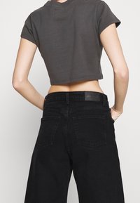 Lyhythihainen musta t-paita, joka on yhdistetty high-waisted mustiin denim-farkkuihin. Farkuissa on brändätty vyötärönauha ja takataskut.