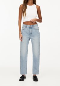 Jeans de mezclilla de color azul claro con cintura alta y corte recto, que presentan bolsillos frontales y cierre de botón, combinados con una camiseta corta blanca.