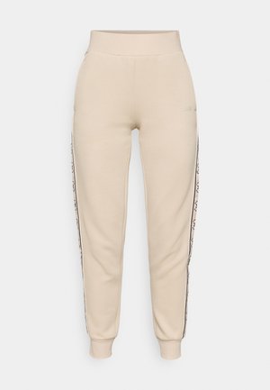 Beżowe dresy wykonane z miękkiego materiału w wąskim kroju, z bocznymi paskami z akcentami logo i ściągaczami u dołu.