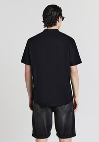 Black short-sleeve shirt with a straight cut and collar, paired with dark denim shorts featuring rolled cuffs and back pockets.