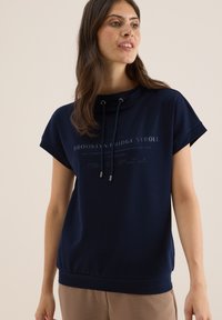 Sweatshirt surdimensionné bleu marine en tissu doux, avec une capuche à cordon de serrage, des manches courtes et un texte imprimé.