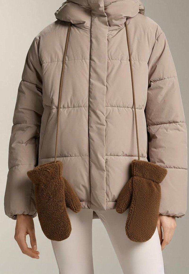 Prošívaná bunda světle béžové barvy s kapucí, s hnědými fleecovými palčáky připevněnými šňůrkami vpředu, zajišťujícími teplo a pohodlí.