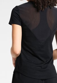 Black T-shirt featuring a sheer mesh back with a triangular design, short sleeves, and a smooth fabric texture.