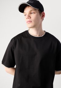 Camiseta negra de manga corta con escote redondeado y detalles en blanco contrastantes. Combinada con una gorra negra con acentos blancos y logo.