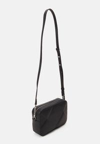 Czarna torba crossbody wykonana z teksturowanego materiału syntetycznego, charakteryzująca się prostokątnym kształtem, zamknięciem na zamek błyskawiczny oraz regulowanym paskiem z metalowymi akcentami.