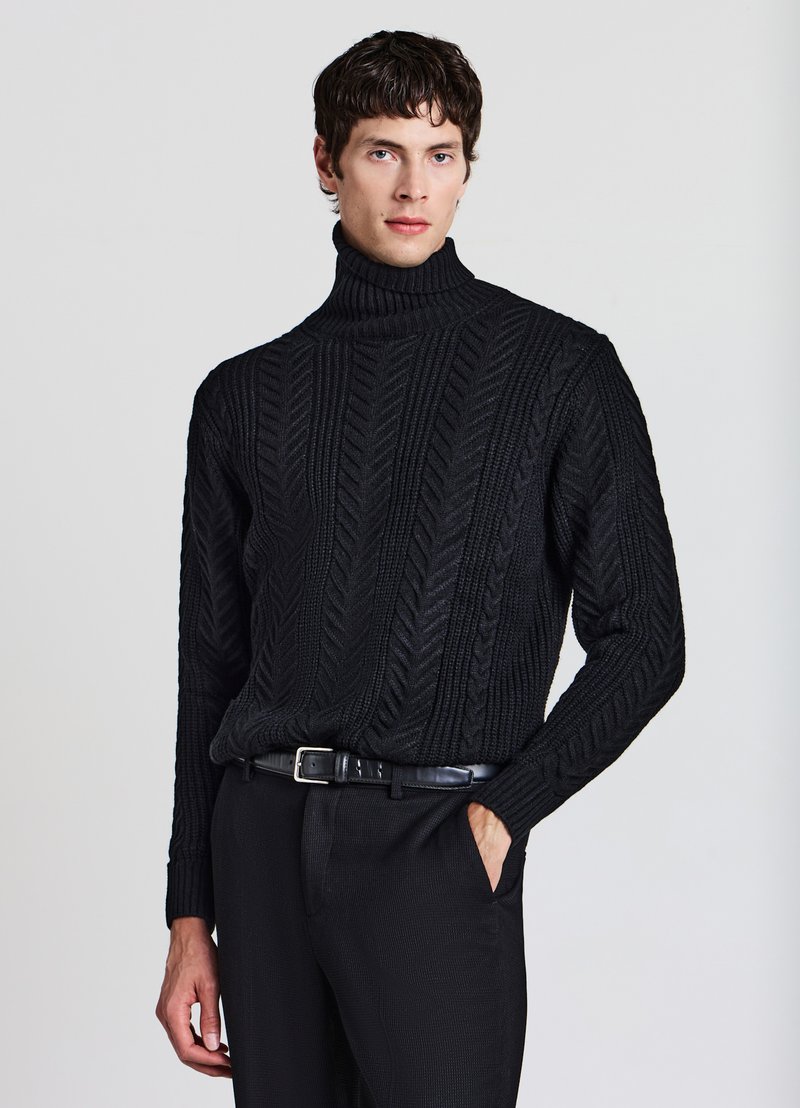Schwarzer Strickpullover mit hohem Kragen und Fischgrätmuster, kombiniert mit schwarzen Hosen und einem eleganten Gürtel.