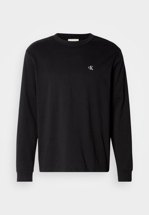 Fekete, hosszú ujjú, kerek nyakú póló, bal mellrészén kis fehér "cK" logóval, fehér háttér előtt bemutatva.