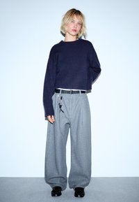 Marinblå kortärmad tröja kombinerad med grå vida byxor och ett svart bälte. Outfiten har en modern, avslappnad silhuett och texturerade tyger.