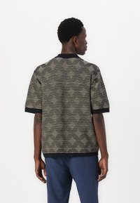 Korte ermelige strikket polo skjorte i svart og beige striper, med en ensfarget svart krage og mansjetter. Teksturert stoff med en uformell passform.