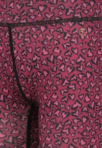 Vaaleanpunaiset legginsit, joissa on sydänkuvio mustana. Sileä pinta, jossa on erottuva musta ommel ja pieni kultainen logotunnus.