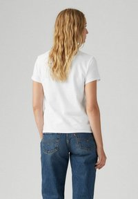 Camiseta de algodón blanca con mangas cortas, cuello redondo y corte relajado, combinada con jeans de mezclilla azul que cuentan con bolsillos traseros y detalles de costura.