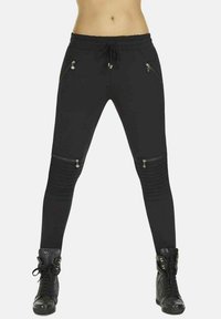 Czarne spodnie sportowe z zamkami błyskawicznymi w kieszeniach, szczegółami w żebrowanym designie oraz elastycznym pasem ze sznurkiem. W zestawie z czarnymi sneakersami za kostkę.